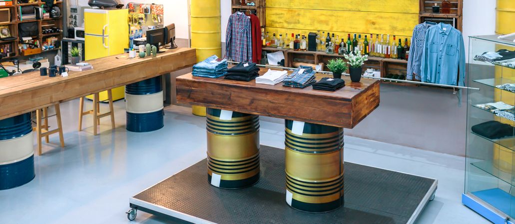 Banner of empty clothing store with clothes on counter over fuel barrels and industrial style
