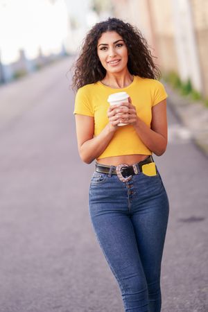 Female in yellow t-shirt walking on street with coffee, vertical composition
