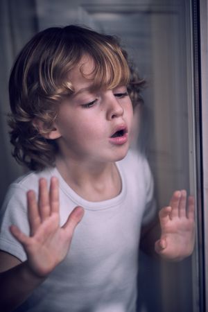 Calm kid blowing on window glass at home