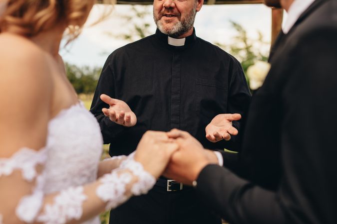Priest giving blessings to couple during outdoor wedding ceremony