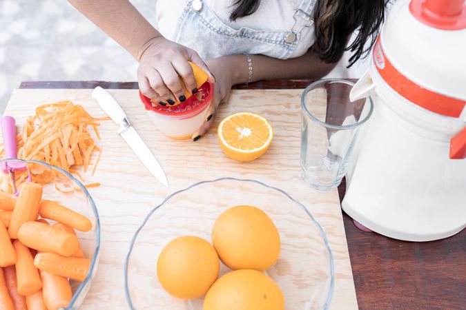 A young Hispanic woman is squeezing an orange to make orange and carrot juice outdoors