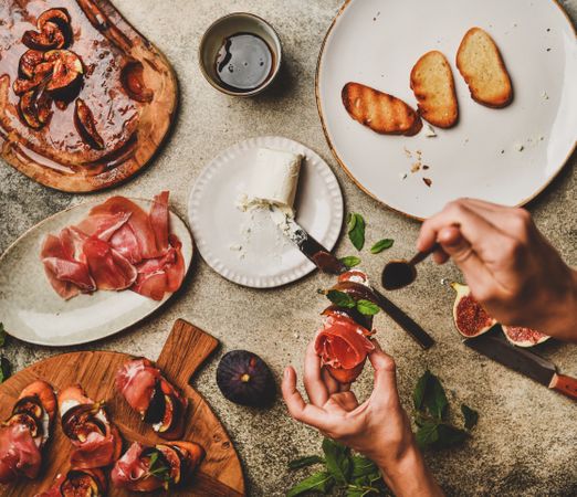 Crostinis with prosciutto, goat cheese and grilled figs, with hands holding spoon, square crop