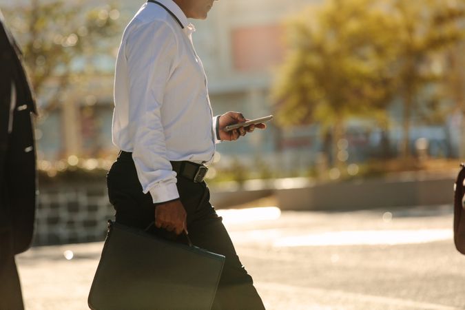 Man using mobile phone while walking on street to office
