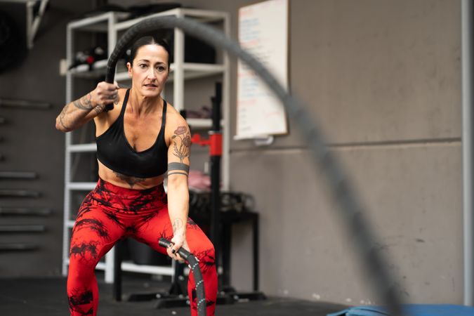 Muscular woman working out upper body with battle rope