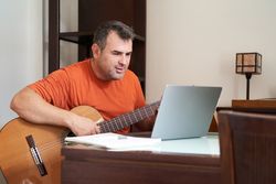 a man with laptop in online guitar lessons learning harmonics