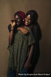 Two African women hugging and laughing against brown wall 4mwBB0