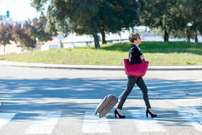 Woman walking confidently across street with roller suitcase behind her