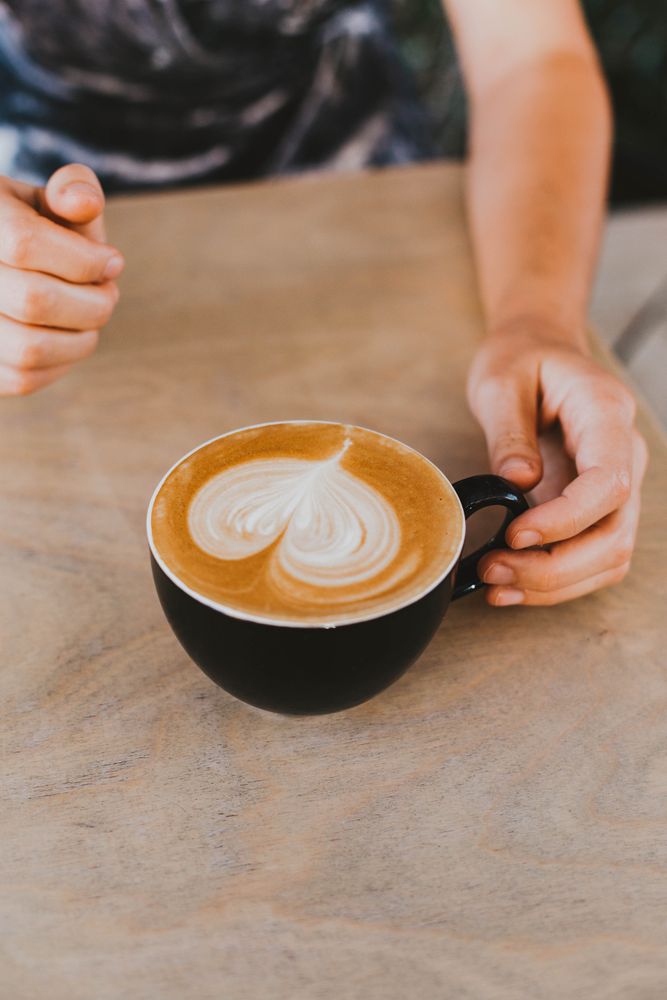 Person holding dark ceramic cup of cappuccino on tabletop
