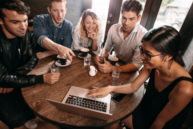 Diverse group of friends sitting together at cafe with man pointing at laptop