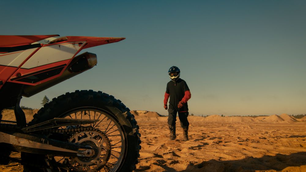 Front View Shot of the Professional Motocross Driver Saddles His FMX Dirt Bike on the Sand/ Dirt Track.
