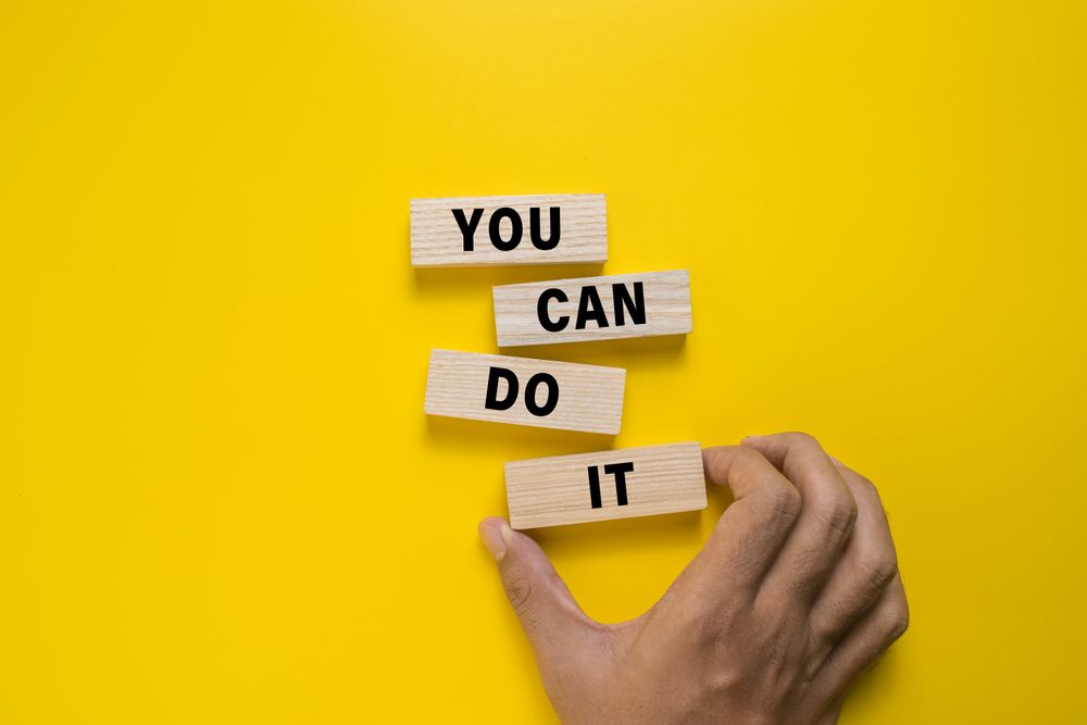 male hand put wooden blocks with you can do it words. isolated on yellow background