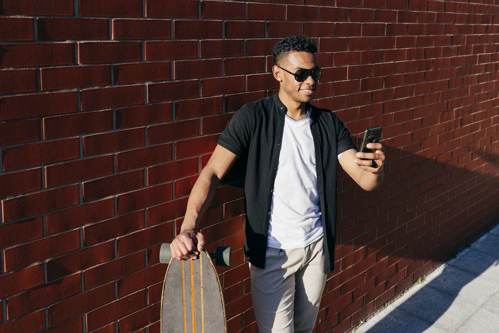 Young Black male with long board speaking on phone