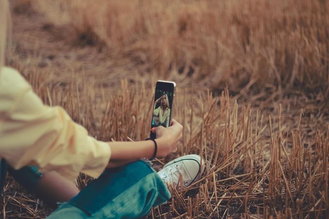 Woman sitting on brown grass taking selfie