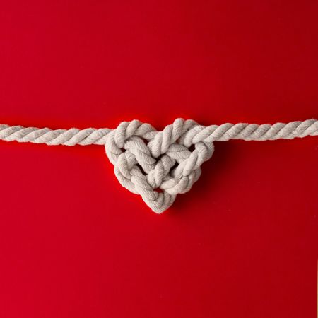Rope in heart shape knot on red background