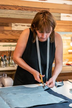 Seamstress using scissors to cut textile at work table. Vertical Shot