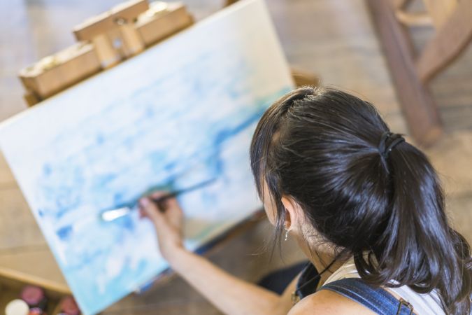 Woman artist painting on a canvas a blue abstract painting. Creative ywoman working on the floor in her art studio.