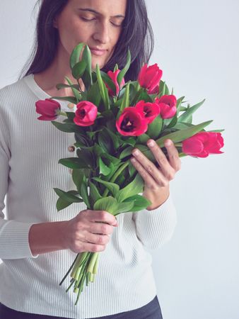 Brunette lady smelling bouquet of red tulips