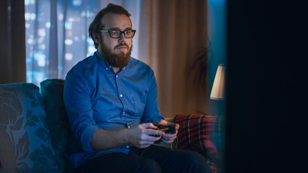 In the Evening Man is Sitting on a Sofa  and Plays in Videogames In His Living Room.