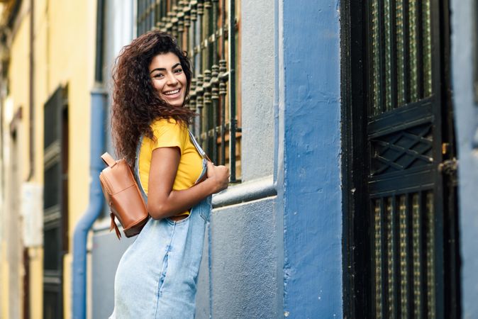 Smiling woman with leather backpack in front of metal door