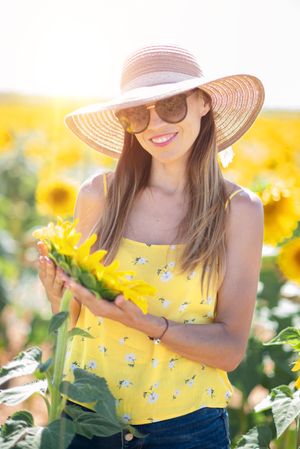 Woman in straw hat gazing while standing on bright sunflower field
