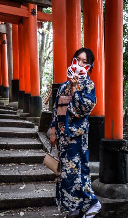 Japanese woman in kimono holding Kitsune mask standing at the red Torii of Fushimi Inari Shrine in Japan