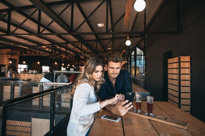 Young man and woman at bar table using mobile phone