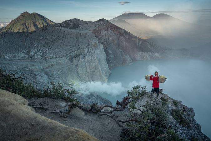 Person holding carrying pole walking near bare mountainous landform in Indonesia