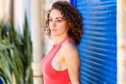 Side view of serious woman standing in front of blue shutters in red vest