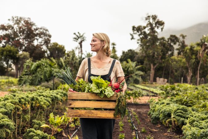 Happy young woman holding a box with fresh produce in her vegetable garden