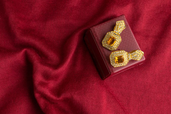 Beautiful shiny golden earrings with diamond studded Indian traditional design on a red velvet background