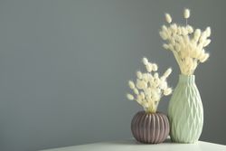 Textured round vase and tall vase filled on table with dried grass in grey room with copy space