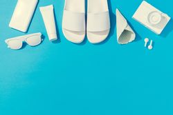 Summer objects of flip flops, sunglasses, camera, smart phone, EarPods on blue background