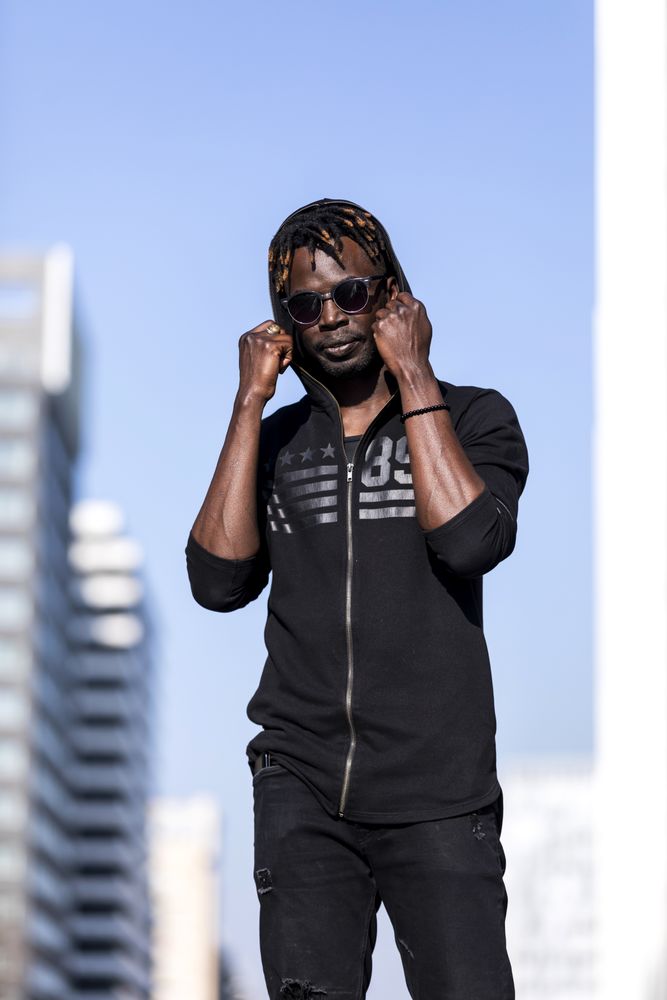 Black man wearing casual clothes and sunglasses standing in the street and pulling up hoodie on sweater