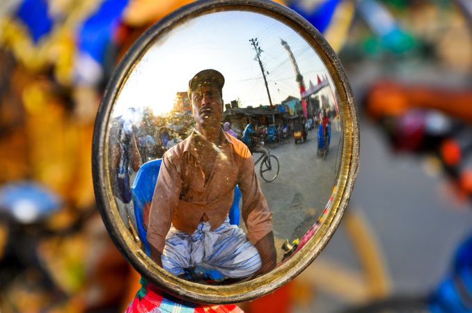 Reflection of man riding a vehicle on mirror in market during daytime