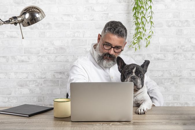 Middle aged man working on his computer beside his dog at home