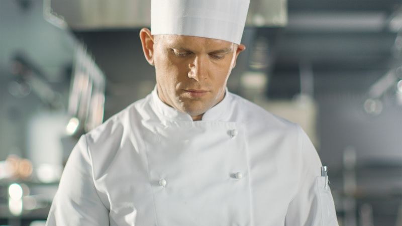 Famous Chef Concentrated on Preparing Fish Dish on a Pan. He Works in a Modern Kitchen.