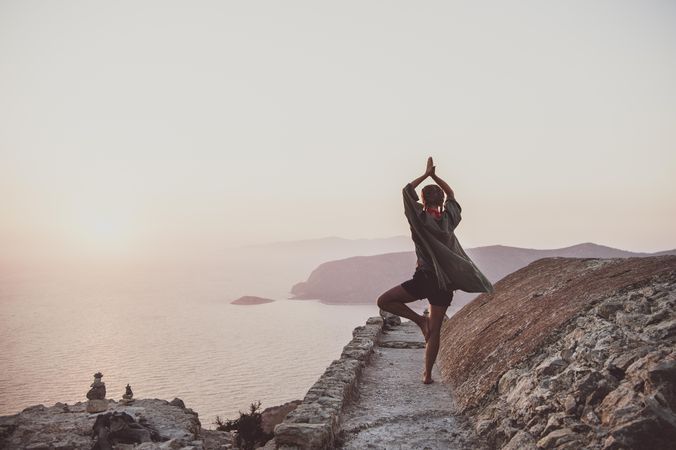 Woman in yoga pose next to castle wall overlooking sea