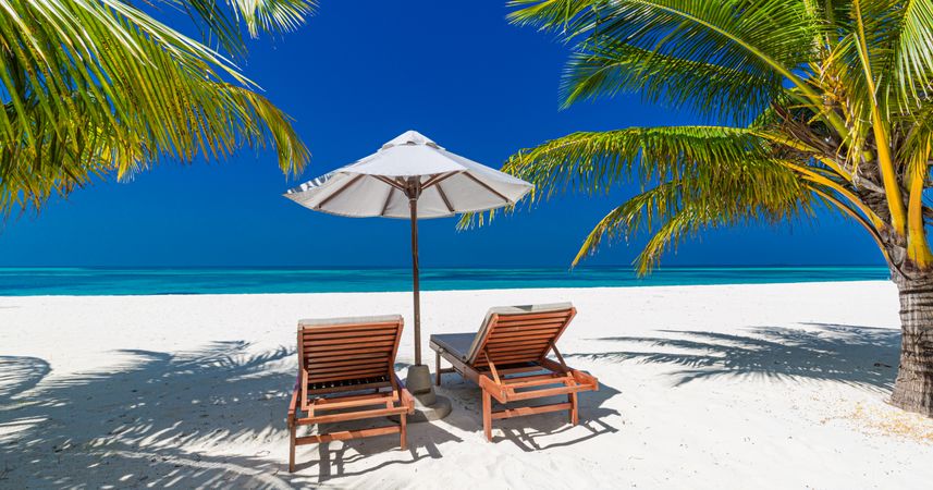 Wide shot of reclining lounge chairs on a tropical beach in the Maldives