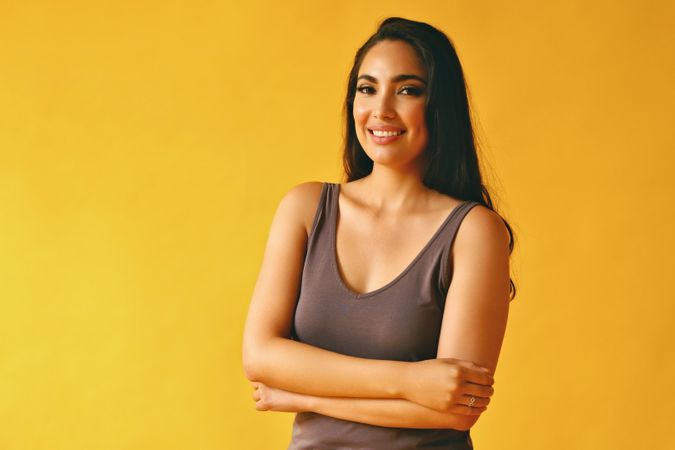 Confident Hispanic woman standing and looking at camera in yellow room, copy space