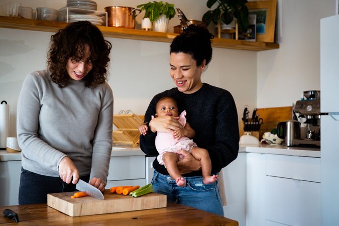 One woman chopping vegetables with other holding baby