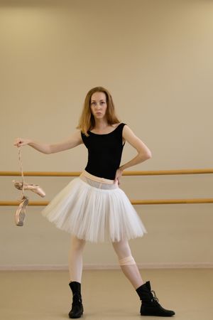 Ballerina holding pointe shoes, wearing tutu and shoes