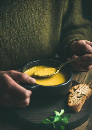 Man eating warm yellow soup holding dark bowl