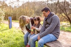 Parents with small girl with drink on park bench in forest