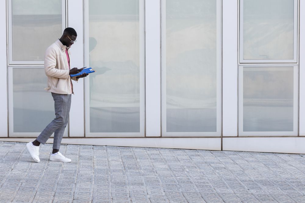 Stylish Black businessman using smartphone in city