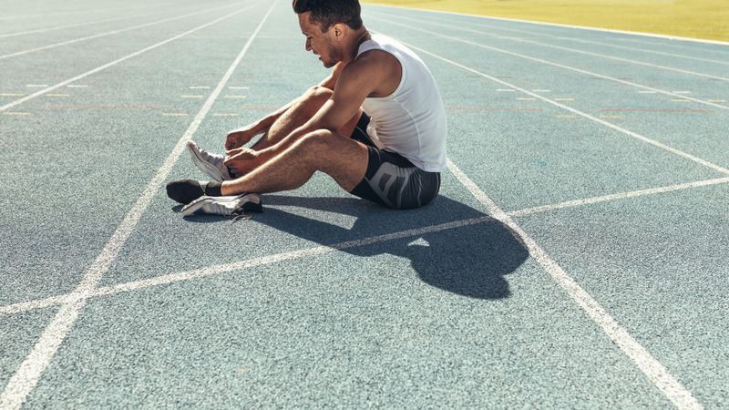 Athlete sitting on a running track tying shoe lace