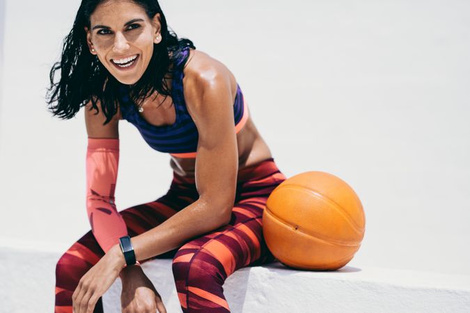 Happy fitness trainer relaxing and sitting next to basketball