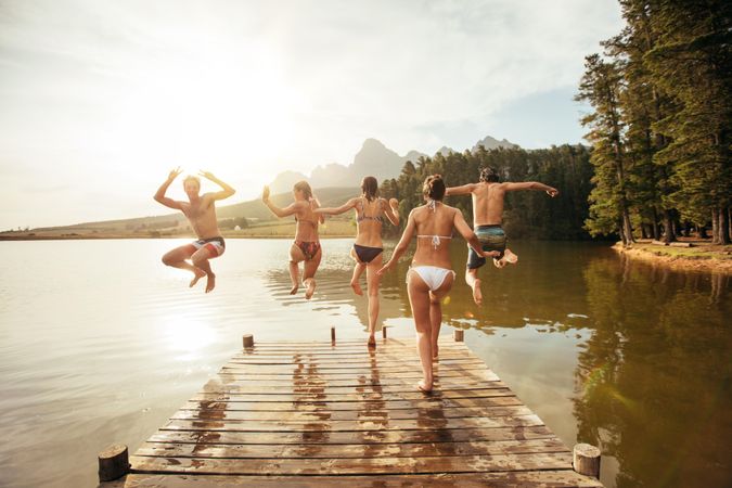 Rear view portrait of young friends jumping into a lake