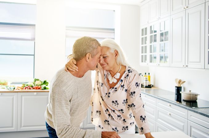 Mature couple with their faces together in a bright kitchen