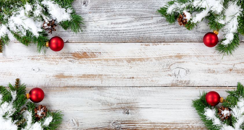 Christmas snow covered evergreen branches and red ball decorations in all corners on vintage wooden boards