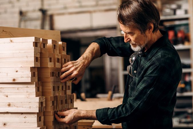 Mature man measuring stack of wooden planks in shop